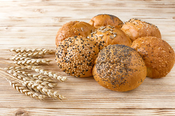 Bread loaf baguette roll lies on the ears of wheat on wood background. flour-bakery yeast, sprinkling of poppy and sesame food