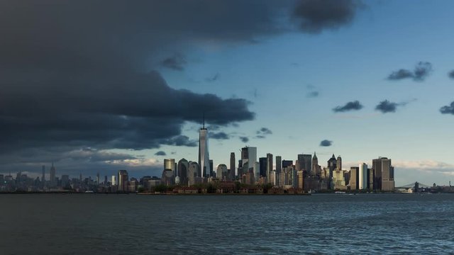 New York City Lower Manhattan cityscape time lapse video with afternoon storm, sunset and city lights at twilight. View of the Financial District skyscrapers, Midtown West and Ellis Island