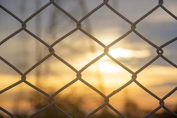 Fototapeta premium selected focus, mesh fence silhouetted against sunset sky with blurr Electricity pylon background