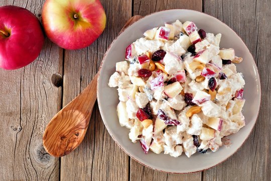 Autumn salad dish with chicken, apples, nuts and cranberries, above on rustic wood background