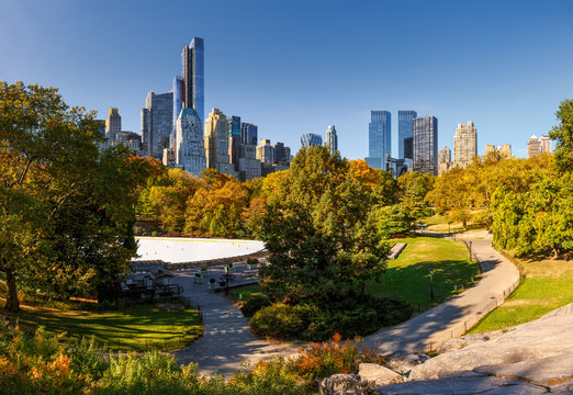 Central Park boasting its fall colors by the skating rink. View of Manhattan Midtown skyscrapers and buildings bordering the park. New York CIty