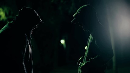 Two hooded criminals in dark park selling buying drugs