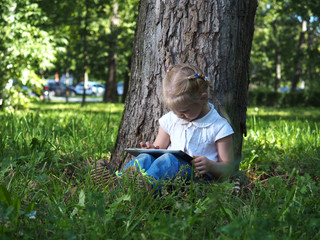 Naklejka na ściany i meble Child with tablet pc outdoors. Little girl on the grass with a computer
