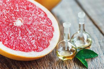 Essential oil in glass bottle with fresh, juicy grapefruit and green leaves-beauty treatment. Spa concept. Selective focus.