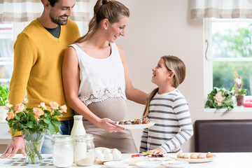 Familie mit schwangerer Mutter, Vater und Tochter backt zusammen in der Küche