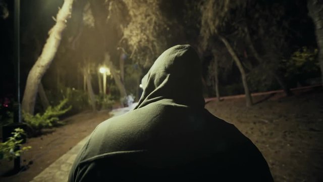 Suspicious hooded figure walks in a dark park at night