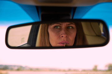woman with lipstick in the mirror of a car