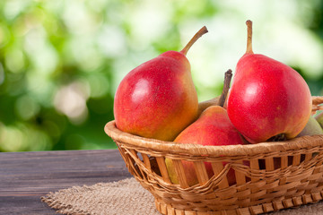 pears in a wicker basket on wooden table with blurred green background