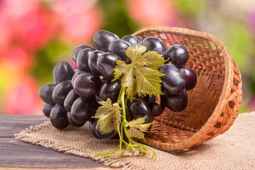 Foto op Plexiglas Blue grapes in a wicker basket on wooden table with  blurred background © kolesnikovserg