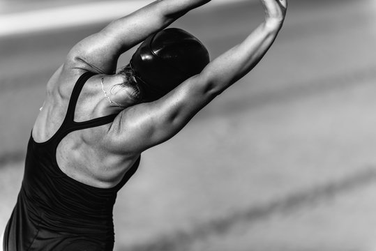 Rear view of attractive woman warming up for swimming by the pool, black and white
