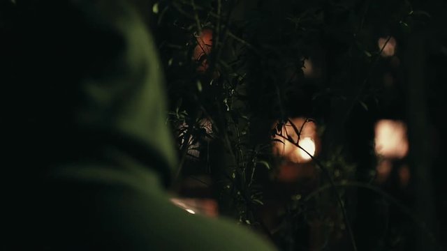 Hooded stalker stalking apartment from a distance at night,rack focus