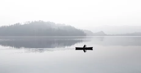 Fotobehang Autumn. Fog over the lake. Silhouette of mountains in the background. The man floats in a boat with a paddle. © patma145