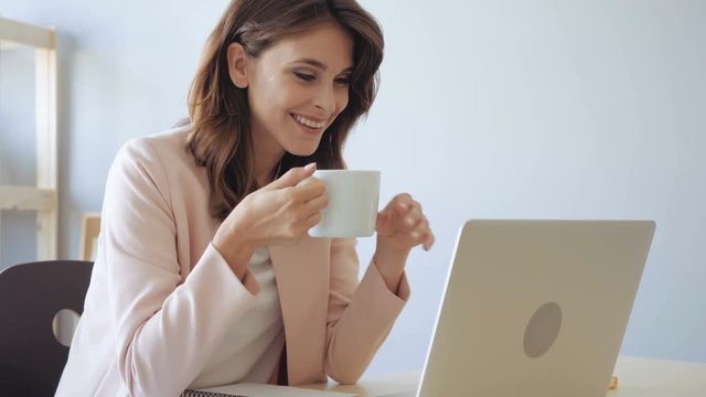 Happy business woman drinking coffee looking at computer display