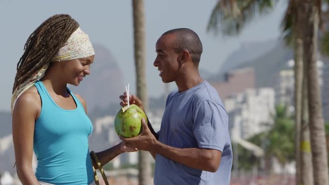 Young brazilian couple walking on the beach drinking coconut