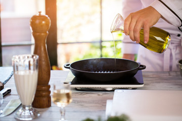 Liquid pours onto frying pan. Male hand holding a bottle. Portable electric cooker. Chef's work in the morning.