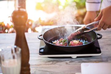 Tongs touch meat on pan. Herbs of green color. Chef prepares beef with thyme. How to cook medallions.