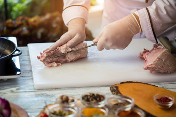 Knife is cutting raw meat. Cook's hands in gloves. Chef is cooking pork. Ingredient of high-calorie dish.