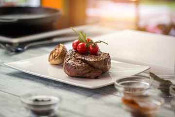 Cooked meat and small tomatoes. Roasted garlic on a plate. Tenderloin steak served at restaurant. Fresh and appetizing.