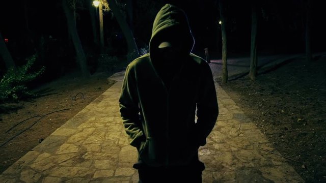 Suspicious hooded figure walks in a dark park at night,100p