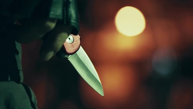 Blade in leather gloved hand shining from the street lights at night