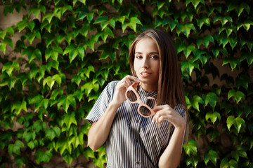 Young beautiful cheerful girl in sunglasses walking around city, smiling. Outdoor background.
