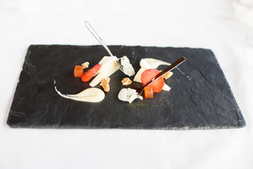 elegant black slate tray with three different asturian cheese for share people, two cheese in pieces and another in little dessert silver spoon, with strawberry pieces, quince and nuts
