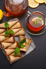 Homemade honey wafers rolled into a cone, filled with condensed milk, a cup of tea and lemon on a black table