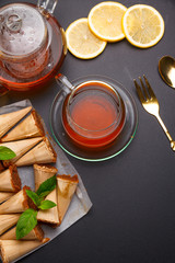 Homemade honey wafers rolled into a cone, filled with condensed milk, a cup of tea and lemon on a black table