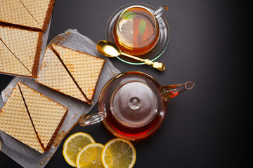 Sweet waffle triangular cakes with condensed milk and fresh hot black tea on a black table