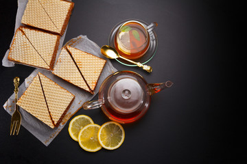 Sweet waffle triangular cakes with condensed milk and fresh hot black tea on a black table