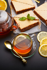Sweet waffle triangular cakes with condensed milk and fresh hot black tea on a black table