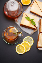 Sweet waffle triangular cakes with condensed milk and fresh hot black tea on a black table