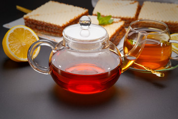 Sweet waffle triangular cakes with condensed milk and fresh hot black tea on a black table
