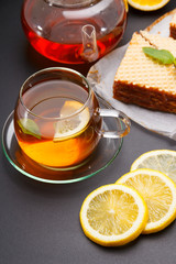 Sweet waffle triangular cakes with condensed milk and fresh hot black tea on a black table