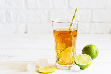 Ice tea in a glass with a slice of lime. White wooden plank back