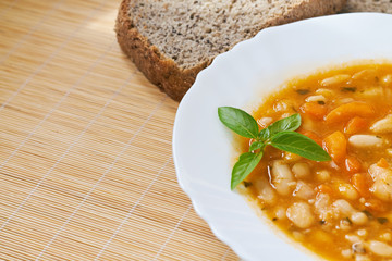 Cooked beans served in white plate with basil leaves and whole wheat bread on wooden background. Plenty of copy space