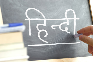 Hand writing on a blackboard in a Hindi class. Some books and school materials.