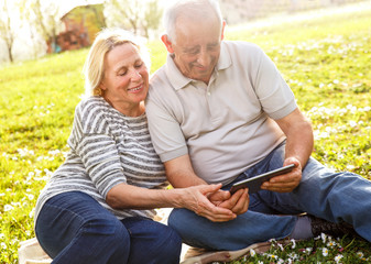 Smiling senior couple in park.They are looking something on tablet.