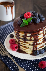 Stack of pancakes with berries and chocolate sauce on a wooden background