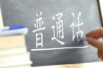 Hand writing on a blackboard in a Chinese class. Some books and school materials.