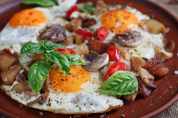 Fried eggs with mushrooms, tomatoes and basil on rustic wooden t