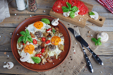 Fried eggs with mushrooms, tomatoes and basil on rustic wooden t