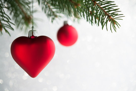 Red christmas ornaments (heart and ball) on the xmas tree on glitter bokeh background. Winter holiday theme.