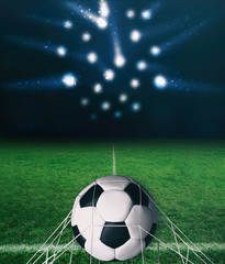 Soccer ball on a green grass on dark background and spotlight with laser rays