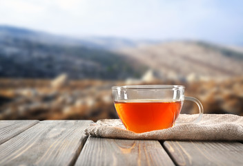 Glass cup of tea on wooden table and blurred nature background