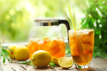 Glass of iced tea on wooden table and blurred green background