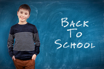 School concept. Cute boy standing on blackboard background. Text back to school.