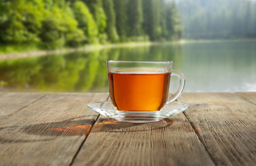 Glass cup of tea on wooden table and blurred nature background