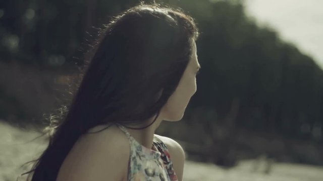 The girl in a flowered dress wakes up on the beach, she runs to the sea and dancing at the water's edge. Then she runs to the fallen tree and begins to walk on it.
