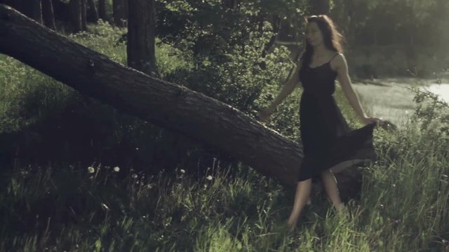 Girl in black dress running through the trees, and then runs to the edge of the cliff and admire the sea.